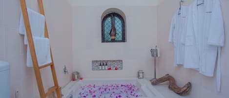 Un bagno con una vasca da bagno piena di petali di rosa, una scala di legno, una finestra e diversi asciugamani bianchi appesi a ganci.