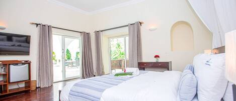 A hotel room with a large bed, a flat-screen TV, a wooden desk, and a sliding glass door leading to an outdoor area.