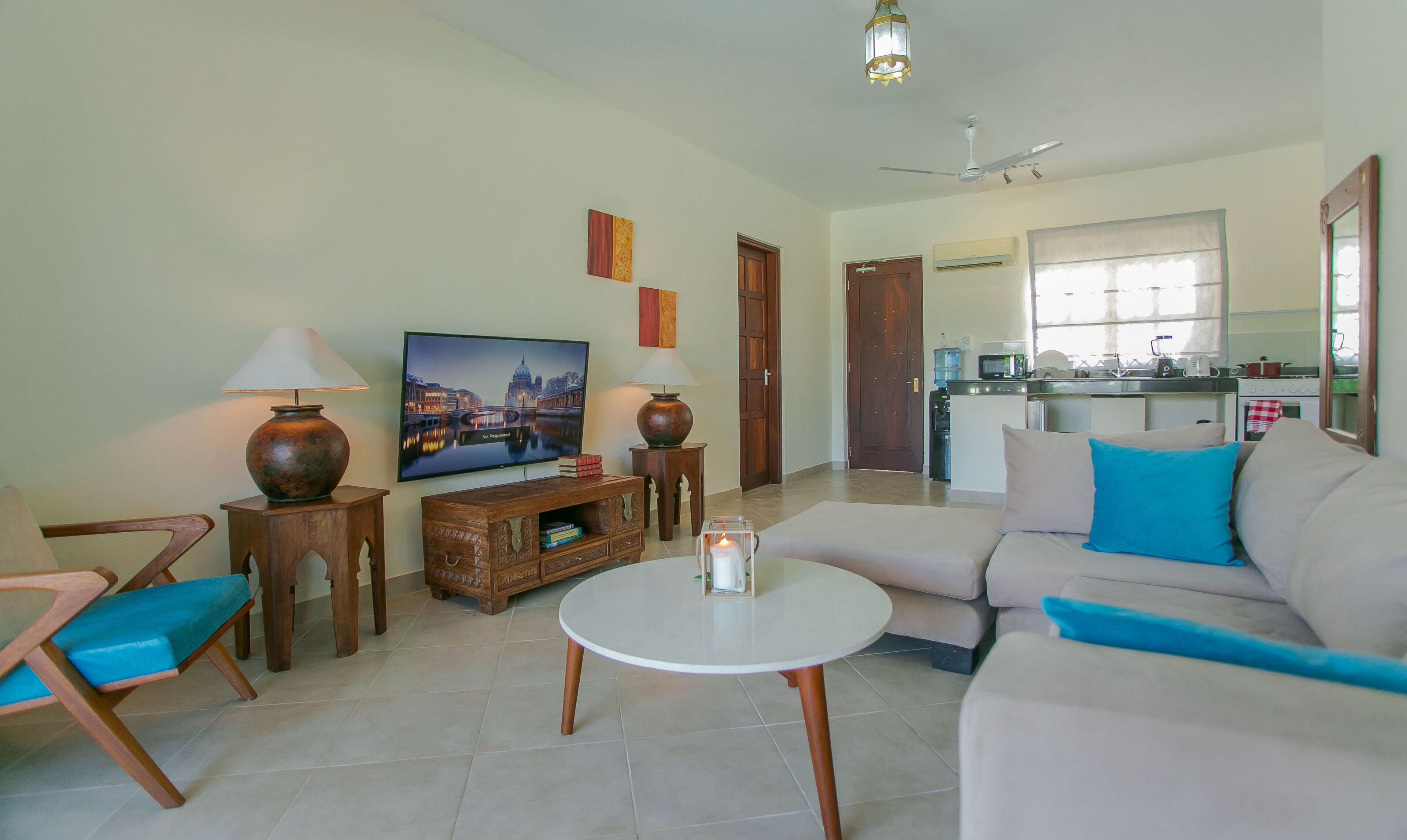 A living room with a sofa, a coffee table, a TV, and a kitchen in the background.