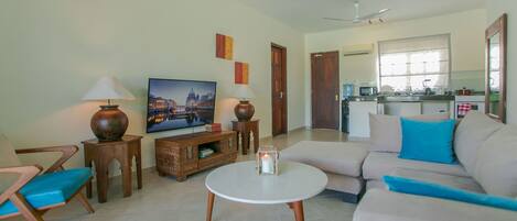 A living room with a sofa, a coffee table, a TV, and a kitchen in the background.