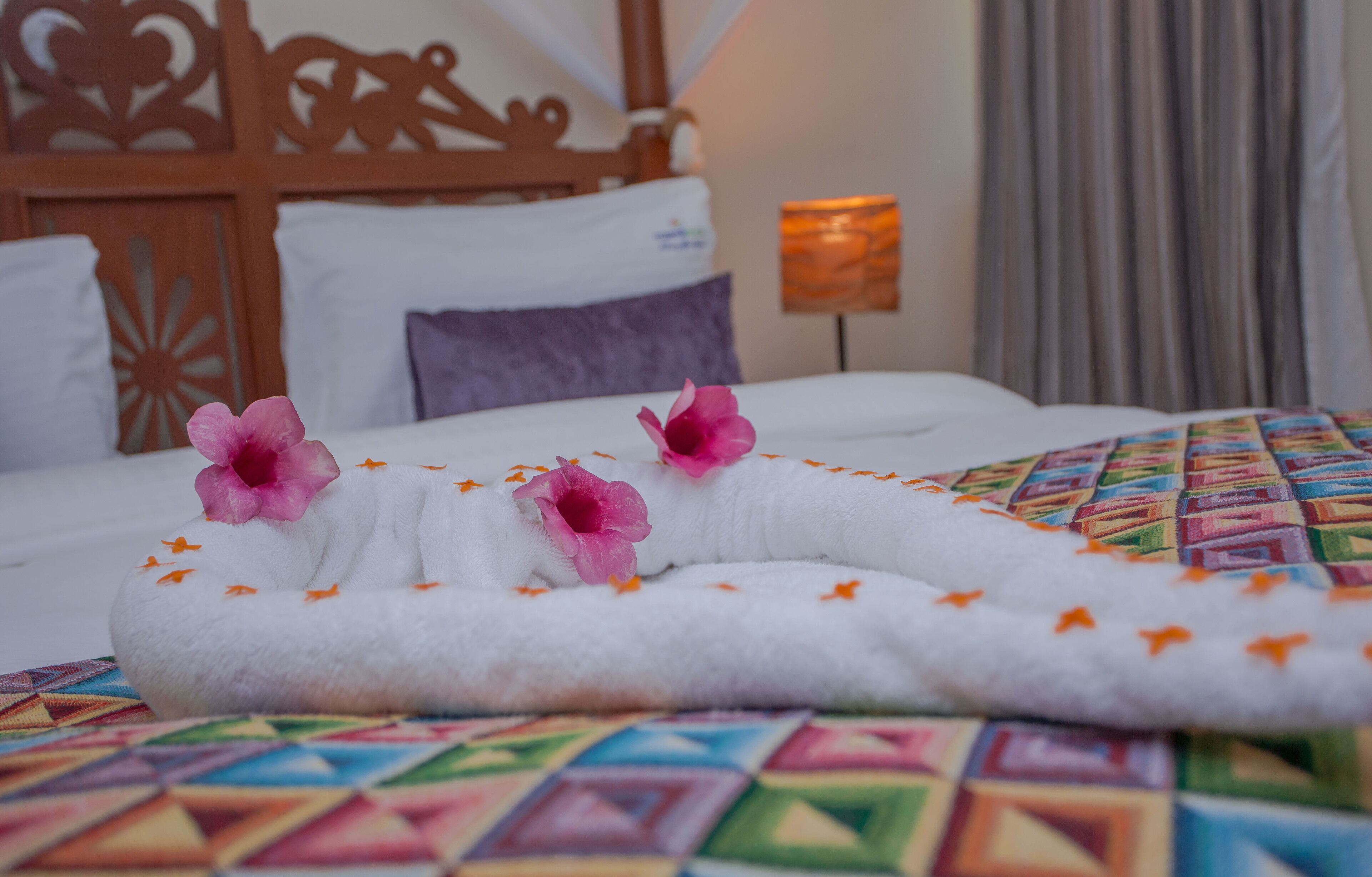 A neatly made bed with a white blanket, pink flowers, and orange accents.