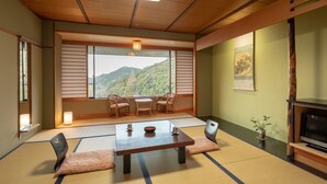 A traditional Japanese room with tatami flooring, a low table with cushions, a television, and a view of a mountainous landscape through shoji screens. - Yamamura Annex (Nagato)