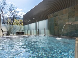 Une piscine extérieure à l’eau claire, un banc et un élément décoratif aquatique.