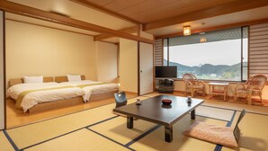 A traditional Japanese-style room with tatami flooring, a bed, a TV, and a view of the mountains. - Yamamura Annex (Nagato)