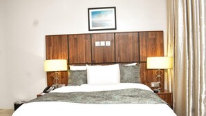 Habitación de hotel con cabecera de madera, dos lámparas de noche, un teléfono y un cuadro en la pared.