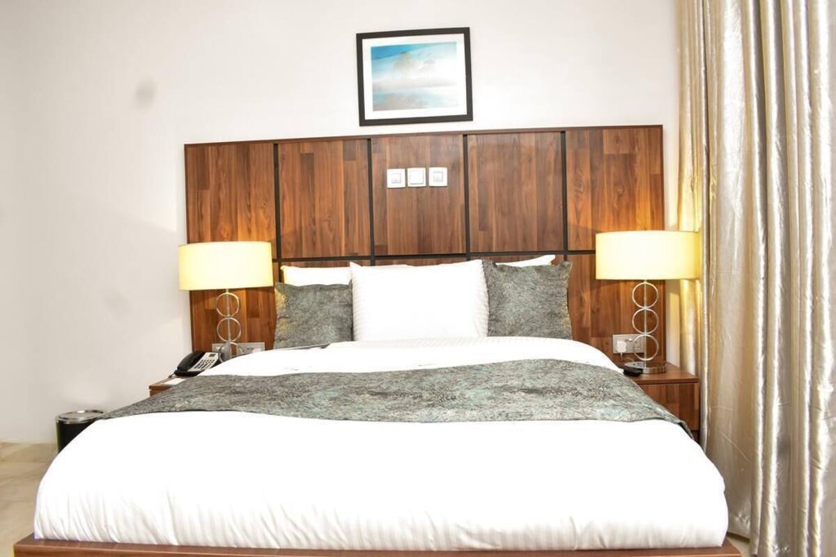 A hotel room with a wooden headboard, two bedside lamps, a telephone, and a framed picture on the wall.