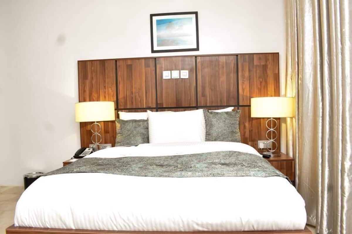 A hotel room with a wooden headboard, a bed with white linens, two bedside lamps, and a framed picture above the headboard.