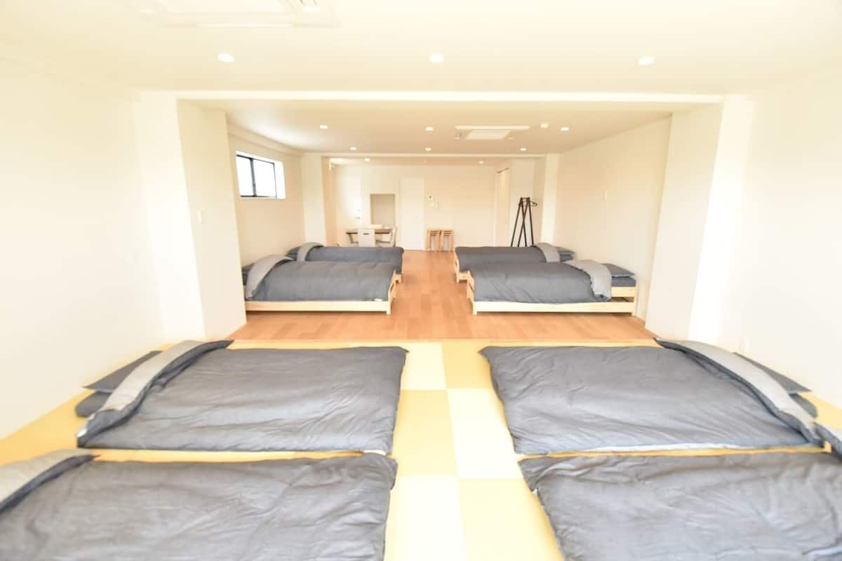 A room with four beds arranged in a row, a desk, and a chair.