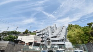 A modern building with a unique stepped design, surrounded by greenery and a clear sky. - Enzo Uno D (Tamano)