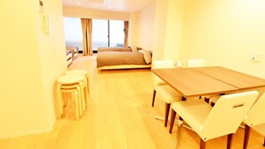 A bright room with a wooden dining table, white chairs, a sofa, and a bed. - Enzo Uno D (Tamano)