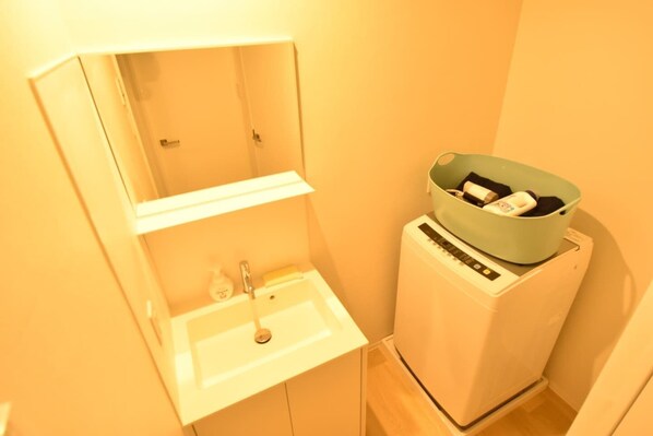 Un baño pequeño con un lavamanos blanco, un espejo y una lavadora.