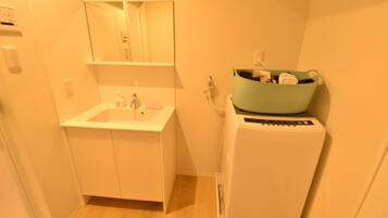 Un baño pequeño con lavamanos, espejo y lavadora compacta.