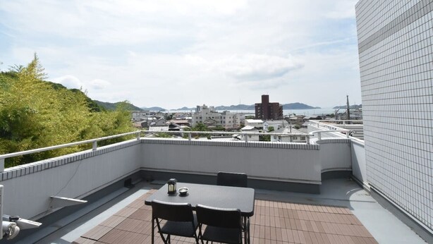 A rooftop terrace with a table and chairs, offering a view of a cityscape and hills in the distance. - Enzo Uno D (Tamano)