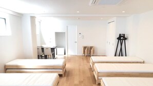 A room with four wooden beds arranged in a row, a desk with chairs, and a tripod in the corner. - Enzo Uno D (Tamano)