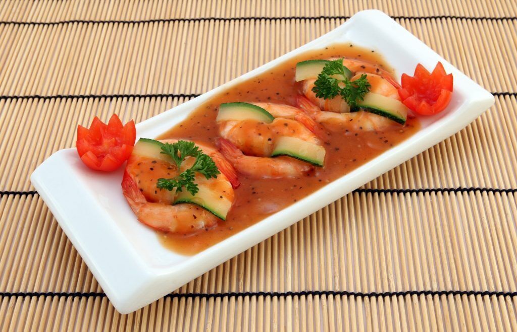 A rectangular white plate with shrimp and vegetables on a bamboo mat.