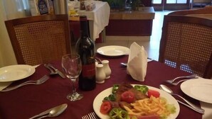 Een eettafel gedekt met borden, bestek, een wijnfles en een maaltijd bestaande uit steak, friet en groenten.
