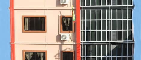 A hotel facade with a sign reading "Royal Landmark Hotel," featuring multiple air conditioning units, windows with curtains, and a tiled roof.