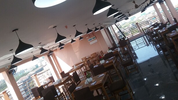 Interior de un restaurante con varias mesas y sillas, iluminación colgante y amplios ventanales que dejan entrar luz natural.