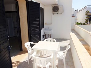 Eine Terrasse mit einem weißen Tisch und Stühlen, einer schwarzen Tür und einem weißen Waschbecken.