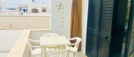 A balcony with a white table and chairs, a brown curtain, and a black door.