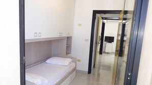 Een kleine, moderne slaapkamer met een enkel bed, inbouwkasten en een inloopkast.
