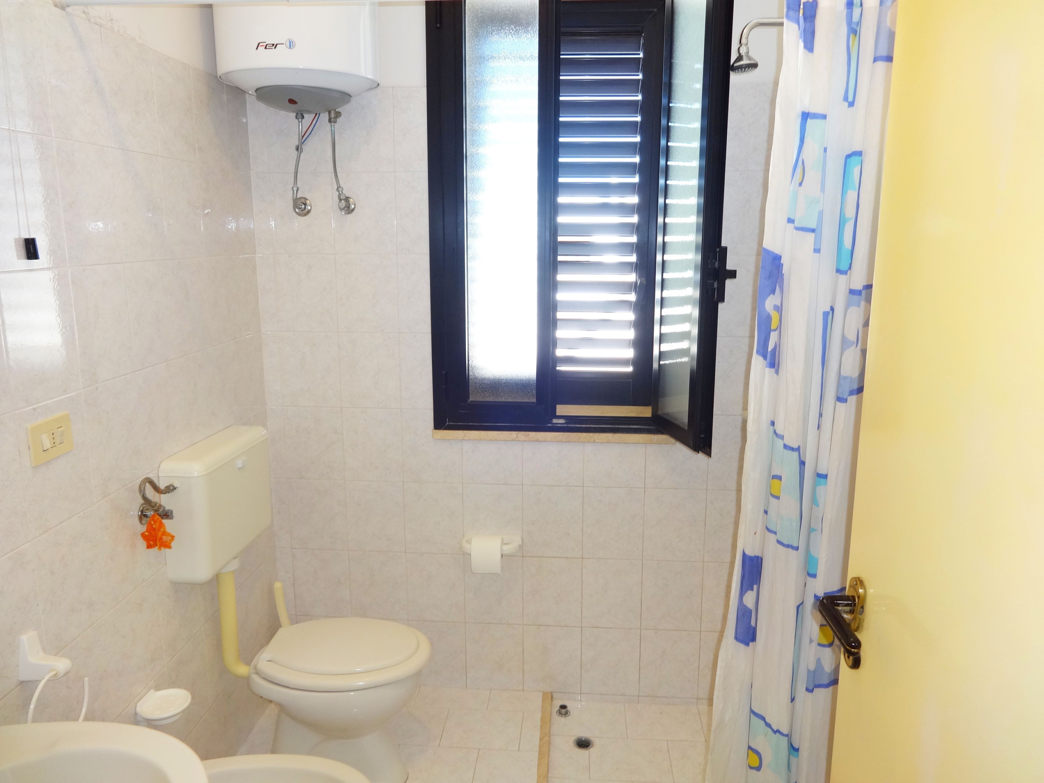 A bathroom with a toilet, a shower area, and a window with blinds.