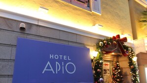 A hotel entrance with a Christmas wreath and lights, a blue awning with the hotel name, and small potted plants at the base. - HOTEL APiO - Adults Only (Tokyo)