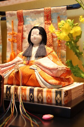 A traditional Japanese doll with a kimono, placed on a wooden base with a patterned cloth backdrop. - HOTEL APiO - Adults Only (Tokyo)