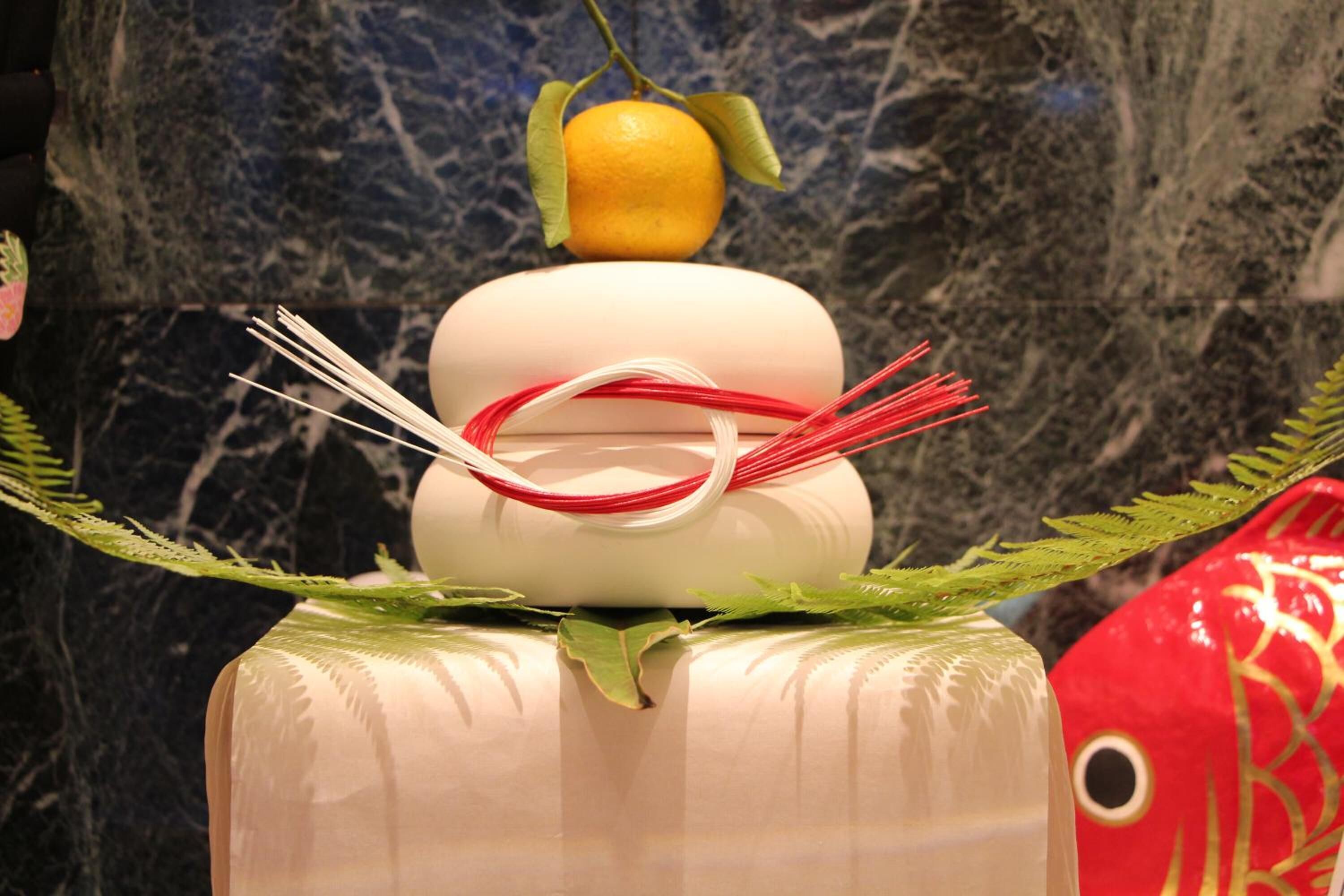 A decorative arrangement with a white cylindrical object, a yellow fruit, and red and white ribbons.