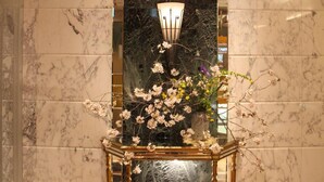 A lobby with a marble floor, a decorative table with flowers, and a wall with a reflective surface. - HOTEL APiO - Adults Only (Tokyo)