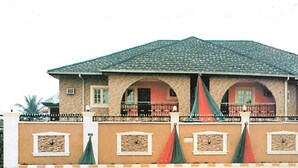 A two-story building with a tiled roof, arched windows, and a balcony with a railing. - Newton Hotel Festac (Lagos)