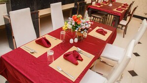 A dining area with tables set for four, each with red tablecloths, white chairs, and a centerpiece of flowers. - Newton Hotel Festac (Lagos)