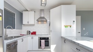 Een moderne keuken met witte kastjes, een roestvrijstalen afzuigkap, een inbouwoven en een vaatwasser.