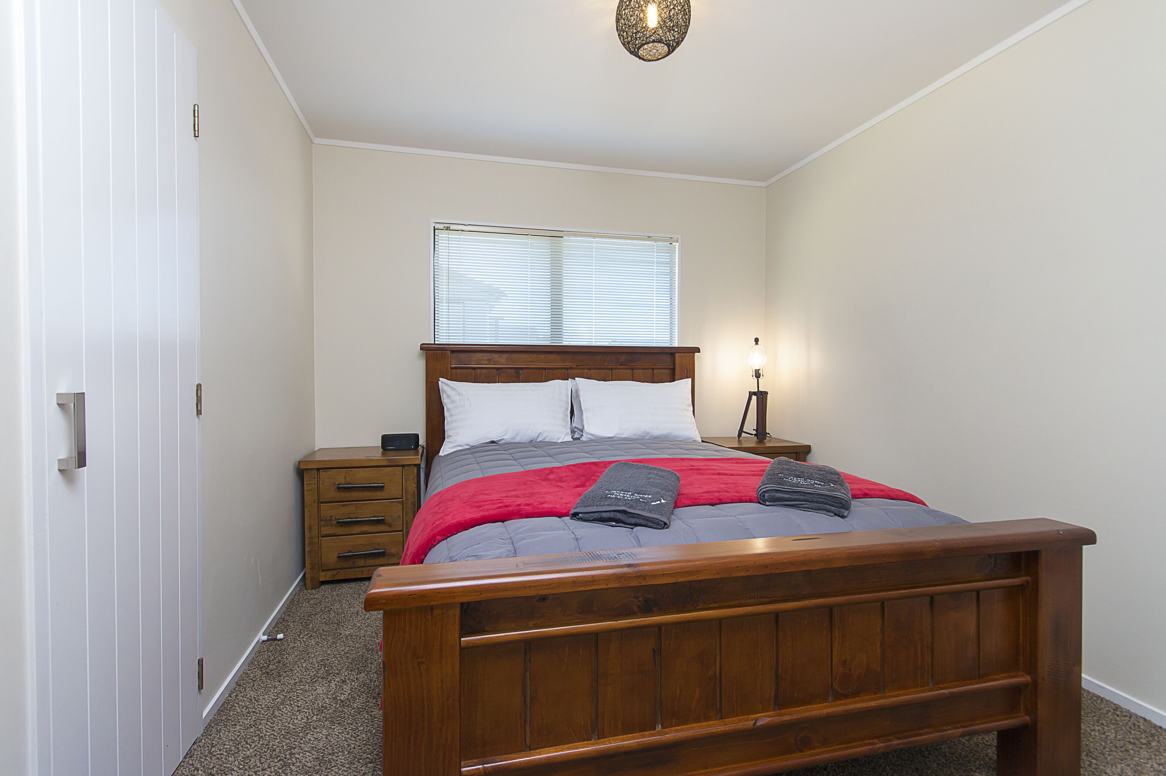 Une chambre à coucher avec un lit en bois, une table de chevet, une commode et une fenêtre avec des stores.