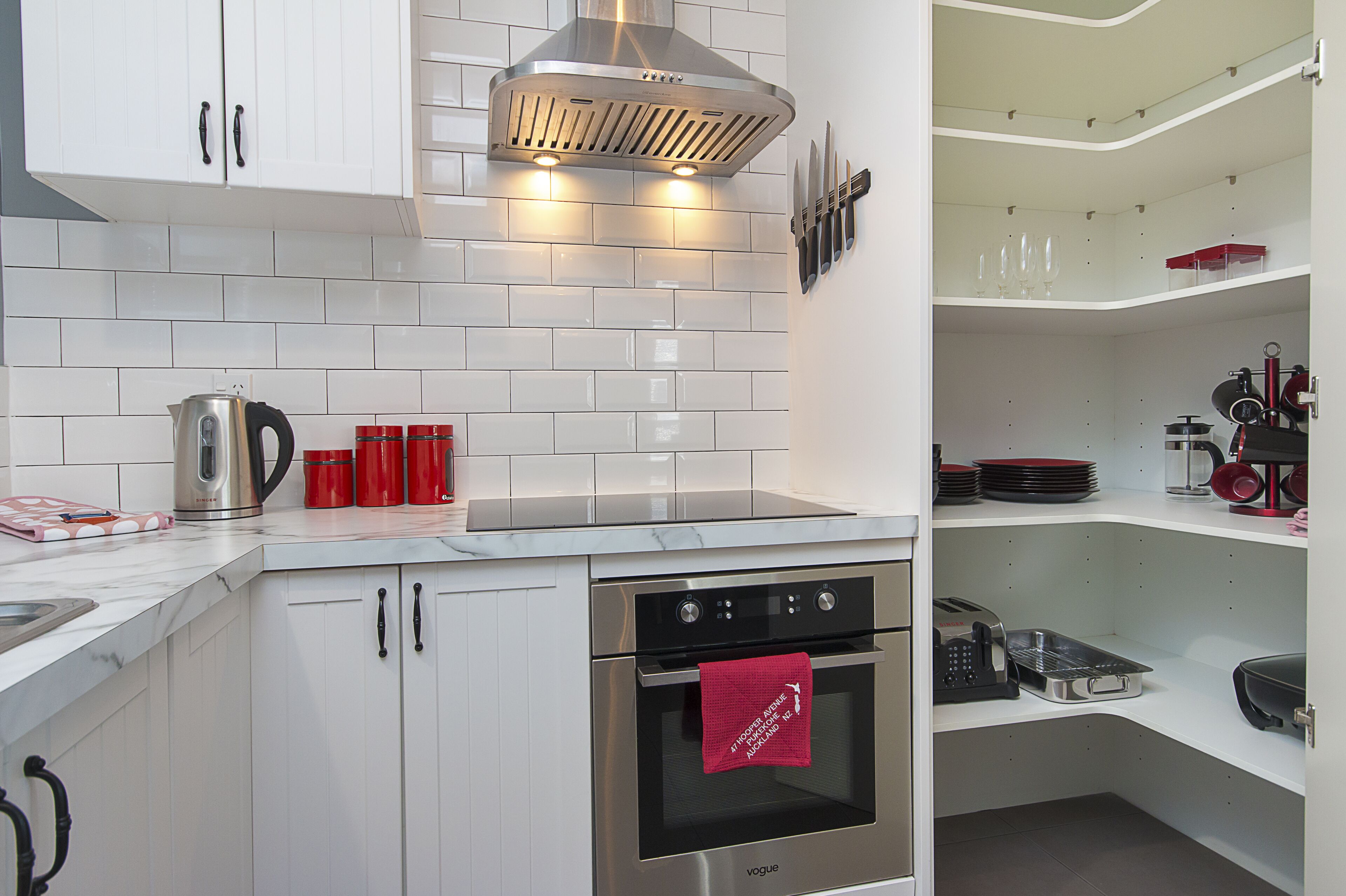 A modern kitchen with white cabinets, a stainless steel range hood, and a built-in oven.