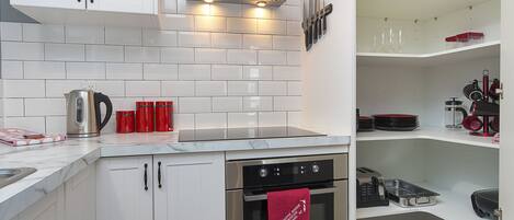 A modern kitchen with white cabinets, a stainless steel range hood, and a built-in oven.