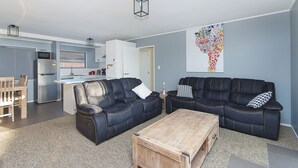 Een moderne woonkamer met twee leren banken, een houten salontafel en een keuken op de achtergrond.