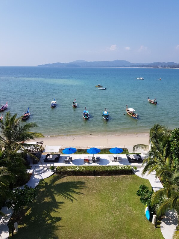 Une vue sur la plage, avec des bateaux sur l’eau, un rivage sablonneux et un espace de détente agrémenté de parasols.