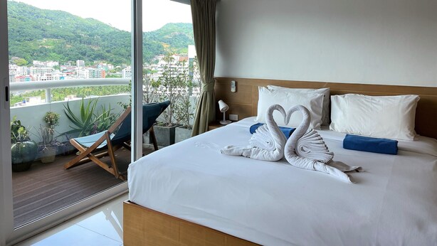 A hotel room with a bed, a view of a cityscape, and a balcony with plants. - Patong Tower by Lofty (Patong)