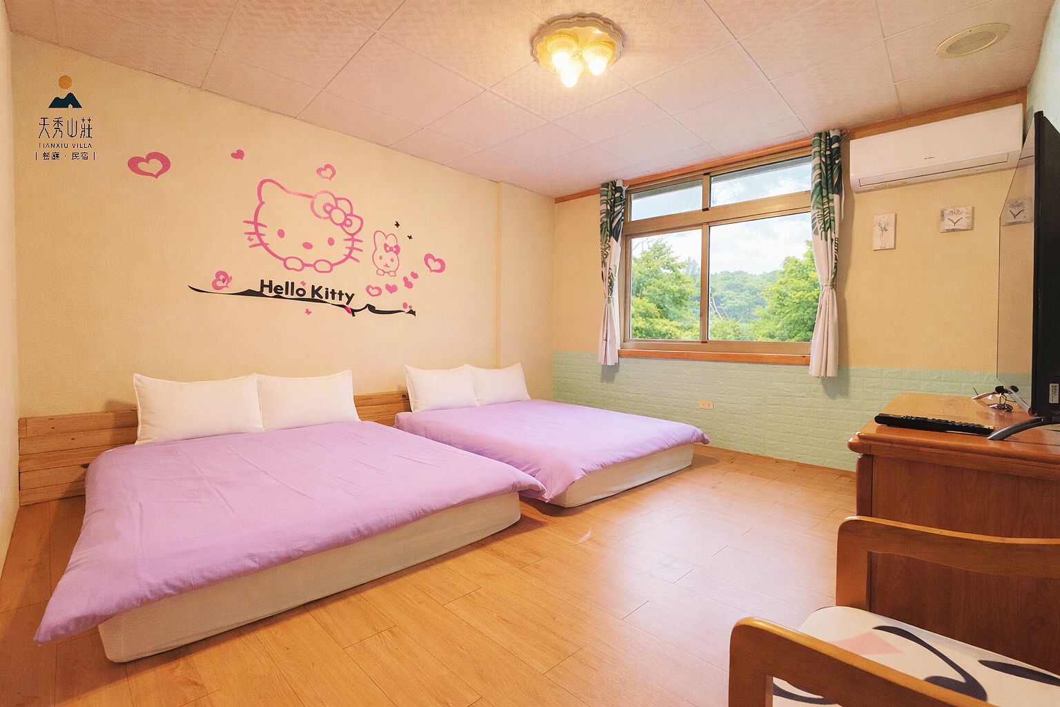 A hotel room with two beds, a desk, and a window with a view of greenery.