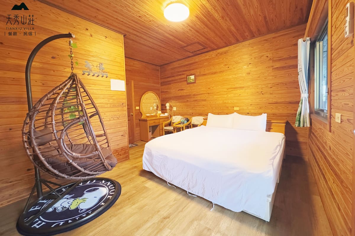 A wooden cabin room with a bed, a hanging chair, a desk, and a mirror.