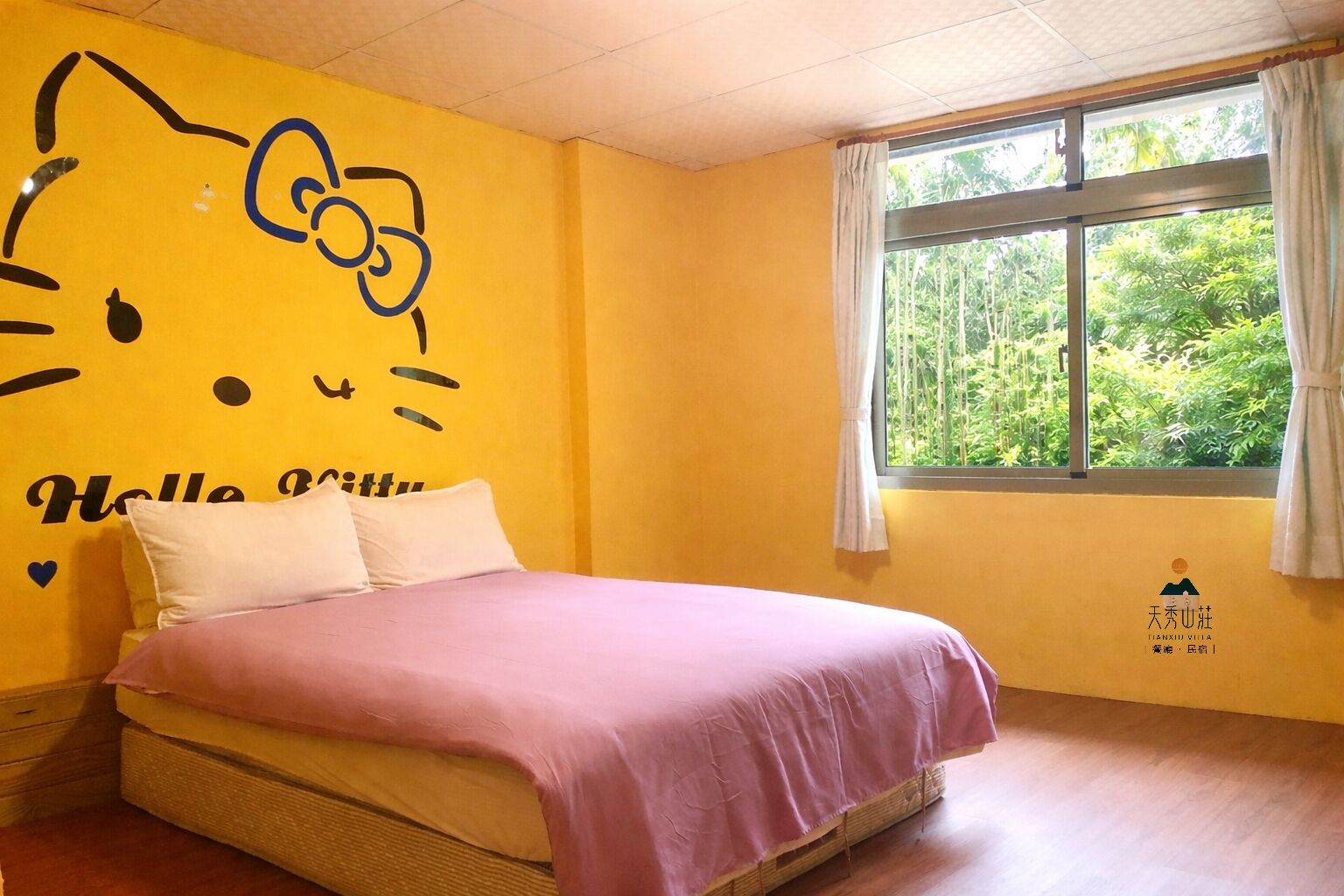A room with a bed, a window with curtains, and a wall with a Hello Kitty design.