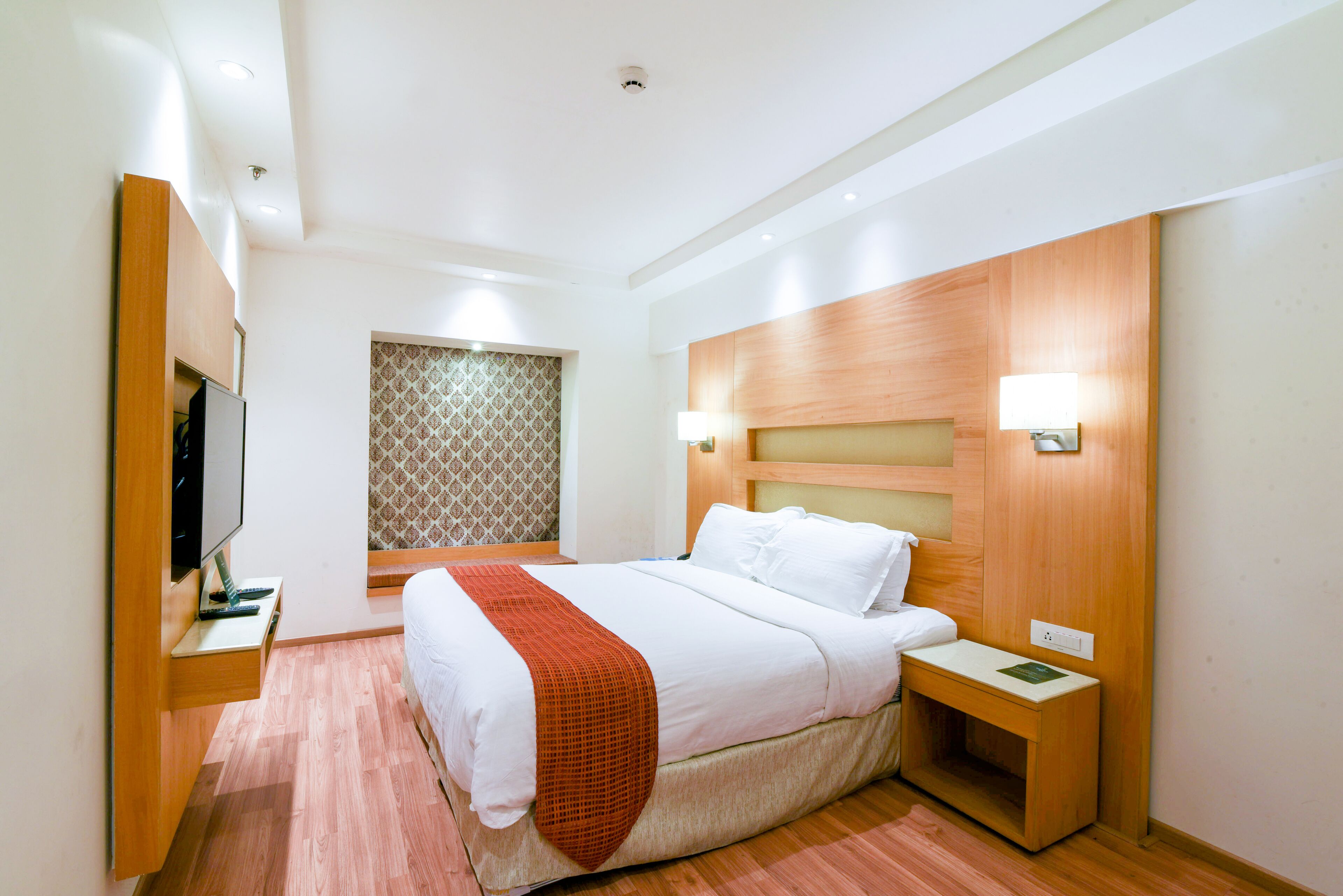 Ein Hotelzimmer mit einem großen Bett, einem Holzkopfende, einem Nachttisch mit Lampe und einem Fernseher auf einem Schrank.
