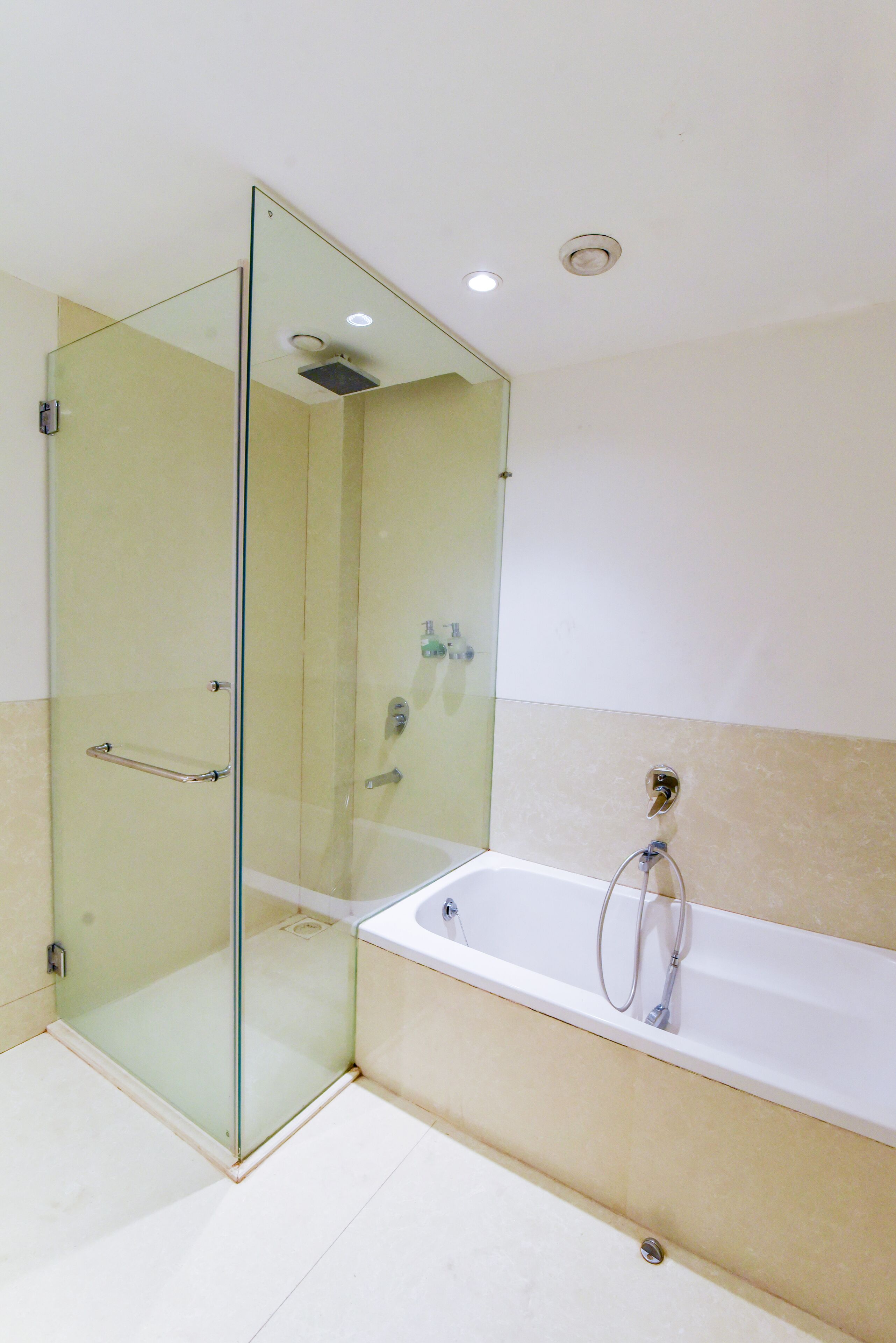 Un baño moderno con ducha envuelta en vidrio, una bañera blanca y paredes cubiertas de azulejos color beige.
