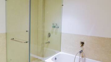 Un baño moderno con ducha envuelta en vidrio, una bañera blanca y paredes cubiertas de azulejos color beige.