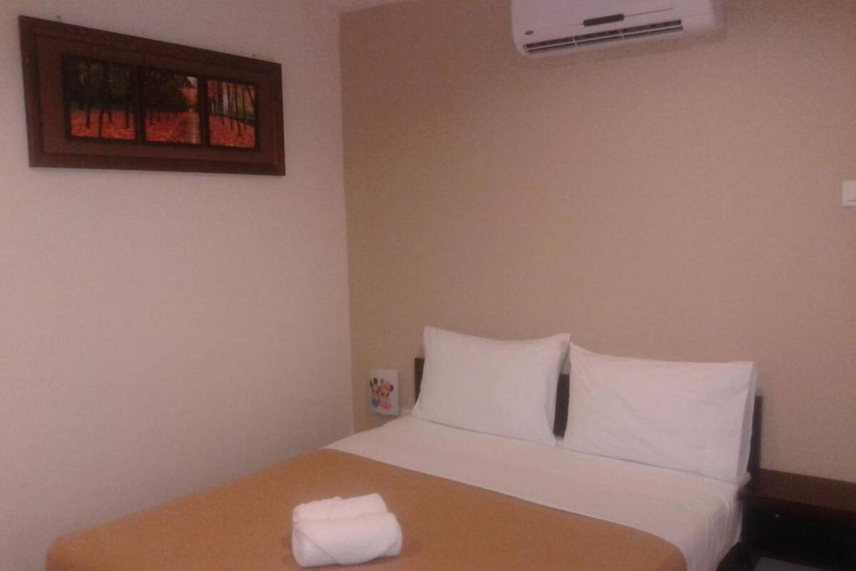 A hotel room with a bed, a painting on the wall, and an air conditioning unit.