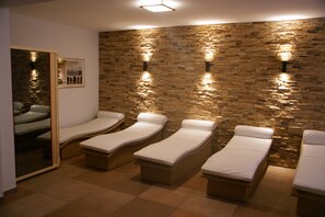 Een spa-ruimte met vier ligbedden, een stenen muur en een ingelijst kunstwerk aan de muur.