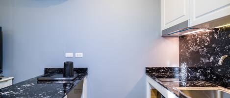 Una cocina compacta con encimera de mármol negro, armarios blancos y horno empotrado.