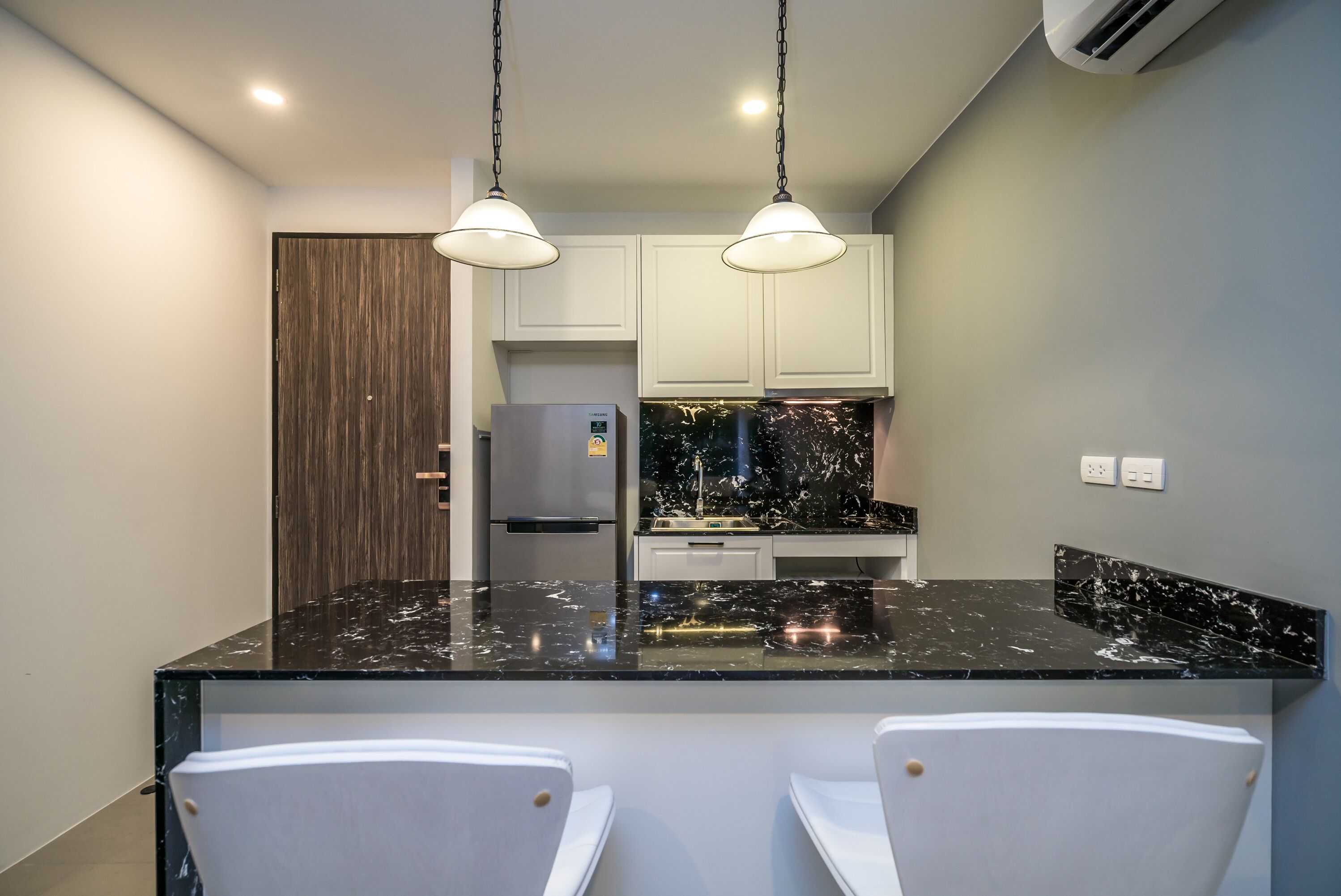 A modern kitchen with a black marble countertop, white cabinets, and two pendant lights.