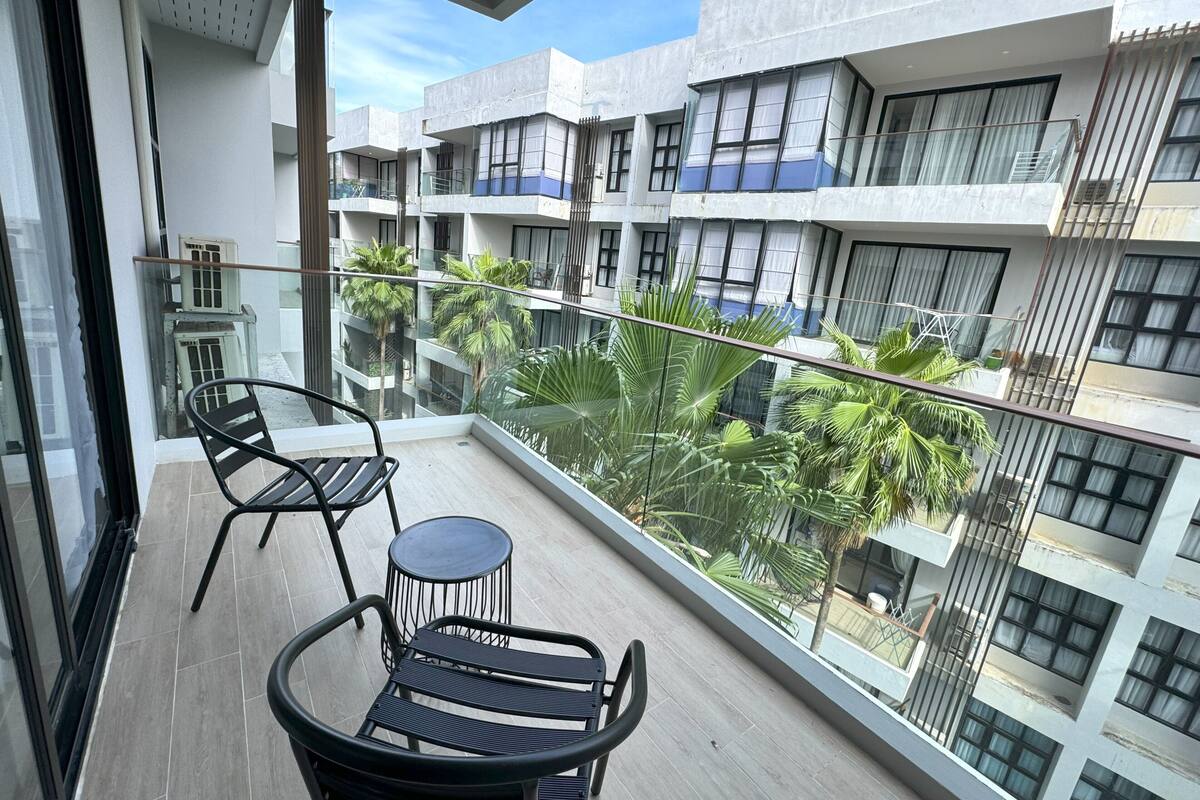 A balcony with two chairs and a small table, overlooking a residential area with multiple buildings and greenery.